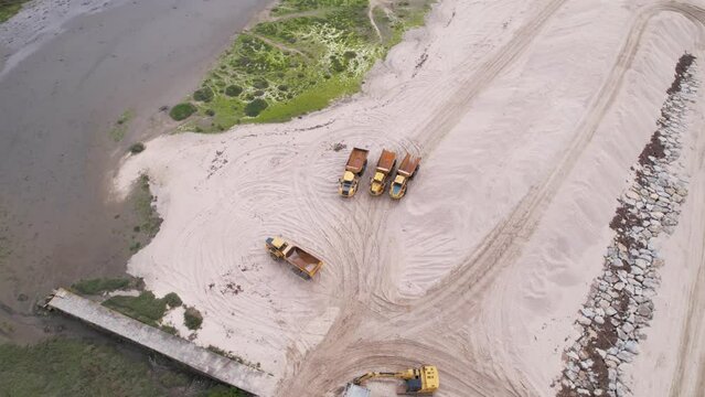 Esposende, Portugal, April 10, 2022: DRONE AERIAL FOOTAGE - The two sides of Restinga de Ofir. Esposende fishing harbor maintenance dredging. Dumper vehicles and rotating excavator parked on the sand.