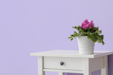 Table with flowers in pot near violet wall