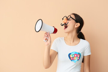 Young woman in funny disguise shouting into megaphone on beige background. April Fools Day celebration