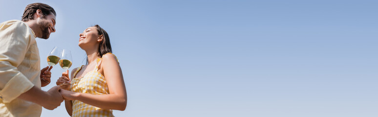 low angle view of young couple in summer clothes clinking glasses with wine, banner.