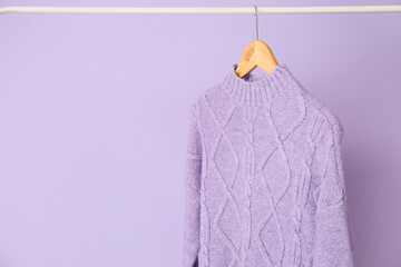 Rack with lilac sweater on color background