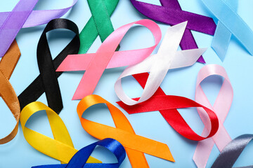 Different awareness ribbons on blue background, closeup. World Cancer Day