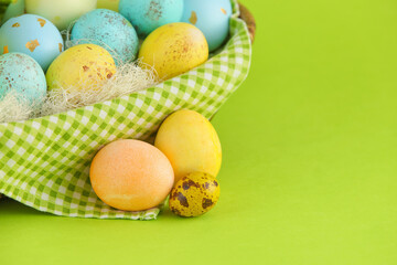 Wicker basket with painted Easter eggs on green background, closeup