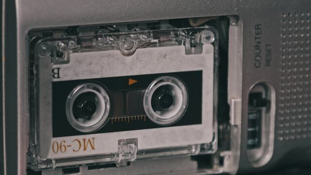Audio Cassette in the Tape Recorder Playing and Rotates. Close-up. Vintage transparent tape with a blank label spinning in the audio player. Call recording on portable handheld retro microcassette.