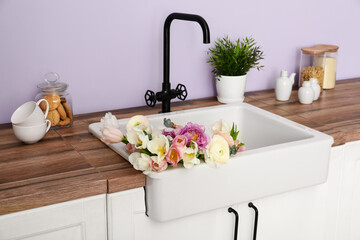 White sink with beautiful flowers and kitchenware on counters near lilac wall