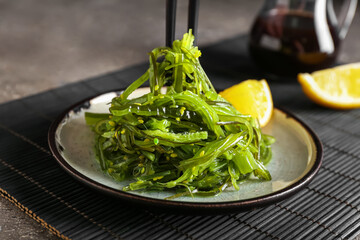 Plate with healthy seaweed salad on grey grunge background, closeup