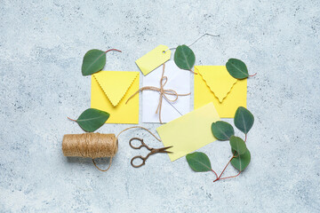 Envelopes with card, tag, rope, scissors and leaves on light background