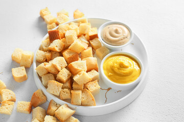 Plate of crunchy croutons and tasty sauces on white background