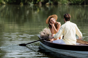 dreamy woman in straw hat looking at romantic boyfriend during boat ride.