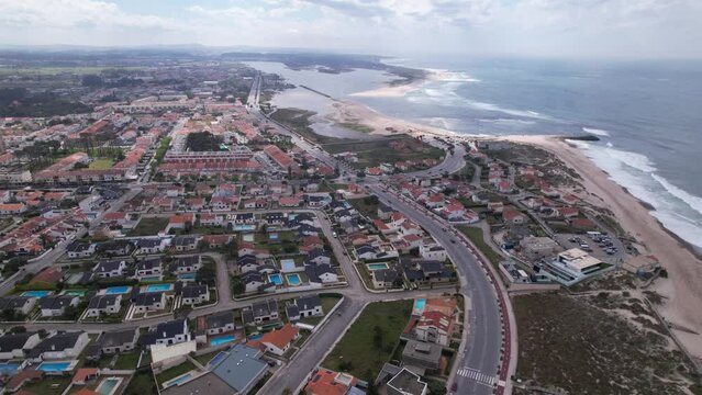 Esposende, Portugal, April 10, 2022: DRONE AERIAL FOOTAGE - The two sides of Restinga de Ofir. Esposende fishing harbor maintenance dredging. Dumper vehicles and rotating excavator parked on the sand.