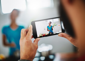 Cooking healthy is easy peasy. Shot of a man filming his wife on his smartphone while she cooks in their kitchen at home.