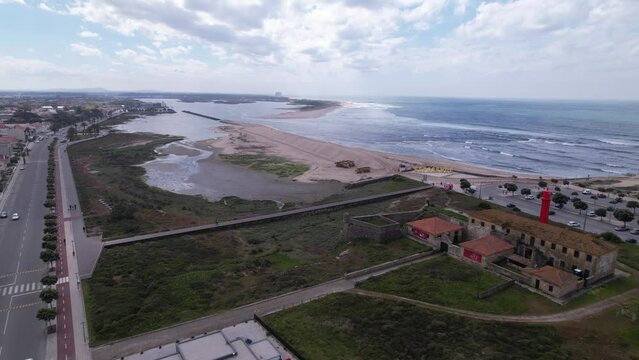 Esposende, Portugal, April 10, 2022: DRONE AERIAL FOOTAGE - The two sides of Restinga de Ofir. Esposende fishing harbor maintenance dredging. Dumper vehicles and rotating excavator parked on the sand.
