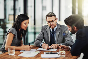 Its a meeting of the minds. Shot of three colleagues sitting around a meeting tablet in the office.