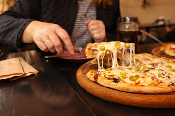 Defocus female hand holding slice of italian pizza Tortilla with grated Mozzarella. Pizza with olives, Basil and cheese close up. Pizzeria outside. Out of focus