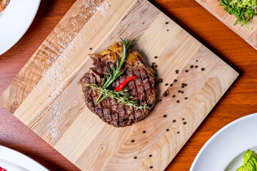 juicy Ribeye steak on the board with rosemary and red chili pepper top view