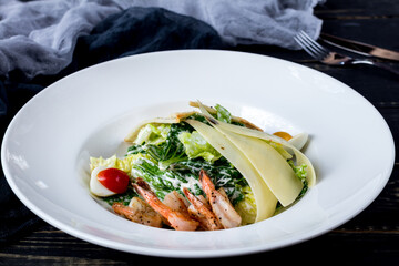 salad caesar with shrimps on white plate on black wooden table