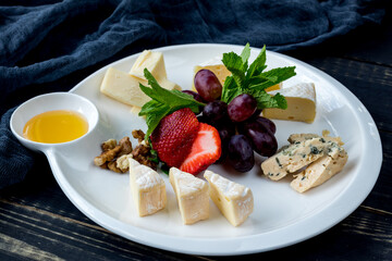 assorted European cheeses on a plate with honey, strawberries, grapes and walnuts with mint