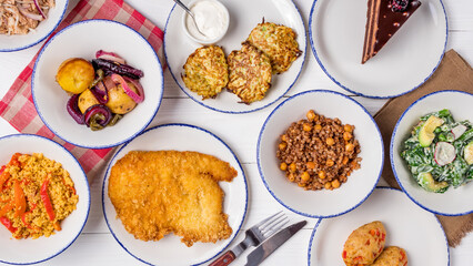 schnitzel from chicken, fried potatoes, salad with avocado, zucchini pancakes, chicken cutlets, chocolate cake and kinoa with vegetables top view on white wooden table
