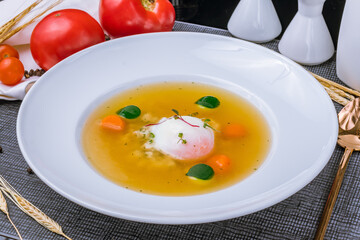 Chicken soup bouillon with poached egg on white plate