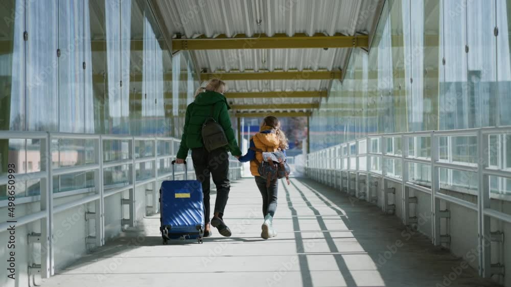 Wall mural Rear view of Ukrainian immigrant mother with child with luggage walking at train station, Ukrainian war concept.