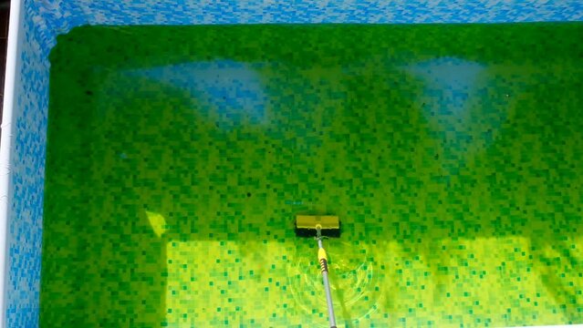 Cleaning the summer pool from green algae.Man brushing a swimming pool .Algae in the pool. slow motion.Pool cleaning tool. 4k footage