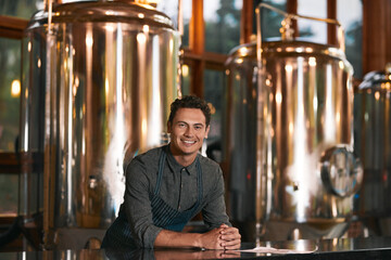 He knows the business in and out. Portrait of a cheerful young businessman seated at a table inside of a beer brewery during the day.