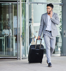 Always on the go. Shot of a young businessman carrying a suitcase while on the phone in the city.