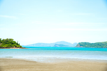 Landscape beach background in Thailand.light blue sky, green mountain background, sea wave and sand beach in pastel style. Concept of summer vacation and holiday tourism.