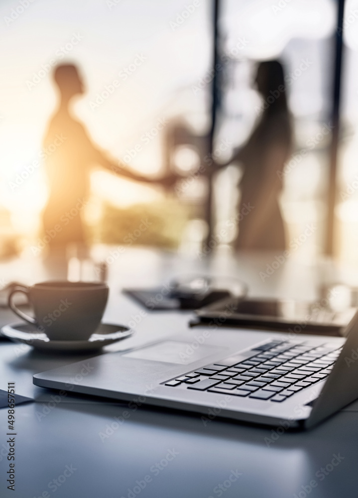 Poster making smart business moves. closeup shot of a laptop on a desk with businesspeople shaking hands in