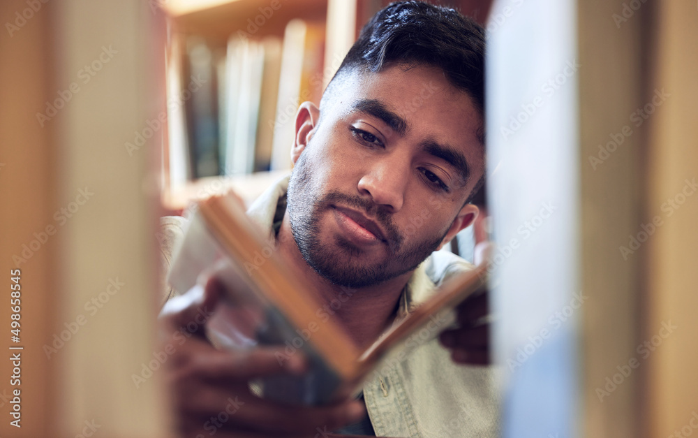 Poster the more pages you turn, the more you learn. shot of a young man choosing a book to read from a libr