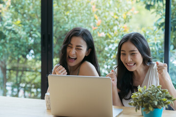 Young two Asian woman celebrating success while working on laptop at home.