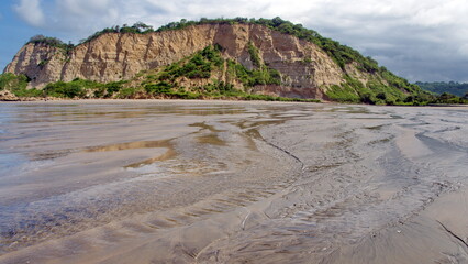 Patterns in the sand of the beach, formed by a river flowing into the sea, beneath a sandstone cliff in Canoa, Ecuador