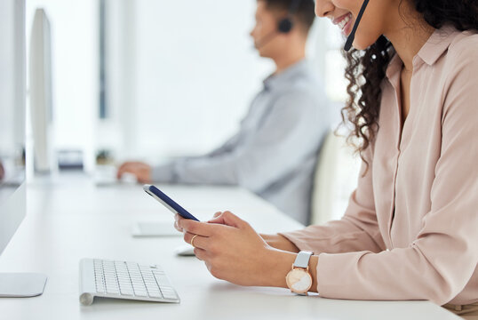 Logging inquiries through multiple digital portals. Closeup shot of a call centre agent using a cellphone while working in an office with her colleague in the background.