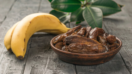Green leaves, dried bananas and fresh bananas on a wooden table.