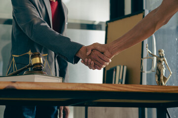 A businessman shakes hands to seal a deal with his partner' lawyer who is discussing the terms of the contract. In front of the hammer and scales, the goddess of justice, the concept of legal counsel.