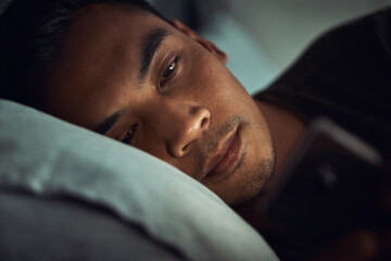 So much for going to bed early tonight. Shot of a young man lying in bed and using a smartphone at...