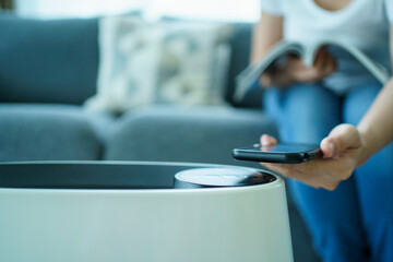 Woman control a modern air purifier through the application on a smartphone