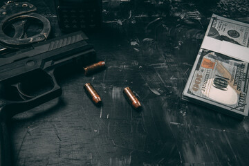 Black pistols, handcuffs, bullets, dollar bills and police radios. Placed on a black wooden table....