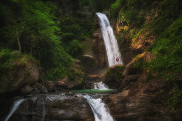 Hiking woman in red jacket stay at big waterfall in mountains.