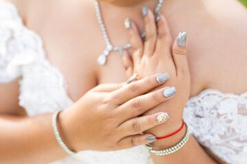 Get a bridal manicure with silver and white nail polish. flowers and glitter Close-up of bride's hands on a bouquet of white roses