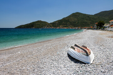 Little fishing boat lying on the beach with crystal clear calm blue water. Mountains in the...