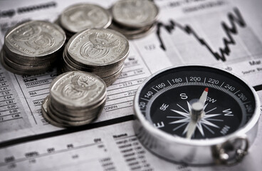 Leading the way to financial success. Studio shot of coins and a compass on the business section of a newspaper.