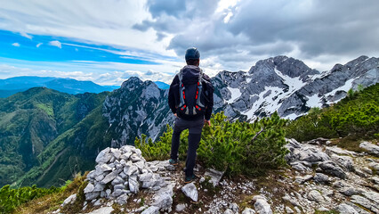 Fototapeta premium Man with backpack and helmet hiking on path with scenic view on mountains Kamnik Savinja Alps in Carinthia, border Slovenia Austria. Velika Baba, Vellacher Kotschna. Mountaineering. Freedom concept
