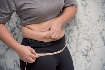 Woman touching stomach holding measuring tape ,Obese  with fat belly in dieting concept. touching stomach holding measuring tape