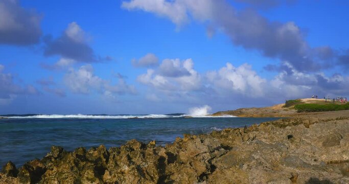 Timelapse of a rocky coastline in the evening druing golden hour. People far in the distance on top of a hill watching the Caribbean sea. Cumulus clouds coming towards.