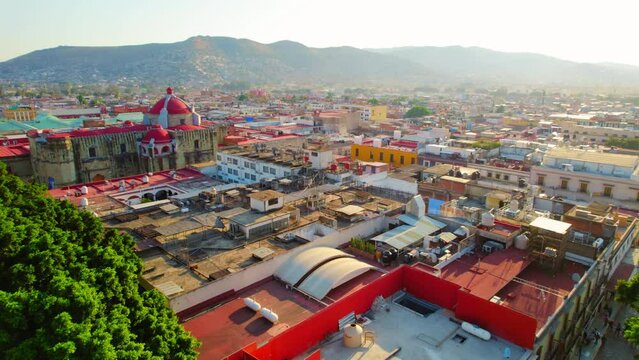 Drone Flying Through Trees Revealing Beautiful Colorful Oaxaca City, Mexico Cityscape During Glowing Golden Hour Sunset.
