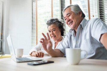 Happy Asian Mature adult couple making online video call and waving hands with their family on Laptop computer.