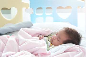 Close up portrait of cute adorable baby girl on white bed in bedroom. Newborn child relaxing sleeping and smiling in the bed in children nursery. Family morning at home.