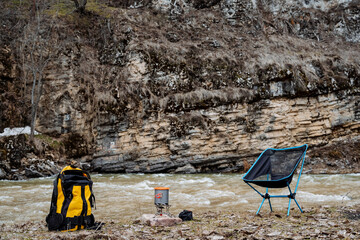 Camping on the river bank, a yellow backpack with hiking equipment, a pot on a gas burner, a...