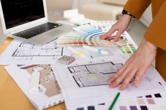Woman architect working on interior renovation in workplace. Designer choosing color samples according to the visualization and blueprints of the project. Architecture and interior design concept.